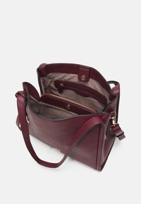 Sac à main en cuir bourgogne avec une finition texturée, comportant une poche zippée dorée, un bouton pression et un intérieur spacieux divisé par des compartiments.