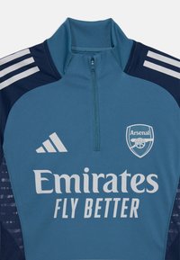 Blauwe sportieve half-zip top met een hoge kraag, voorzien van grijze strepen, het Adidas-logo en het Arsenal-embleem. De tekst luidt "Emirates Fly Better."