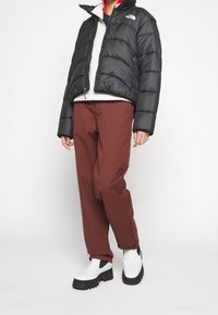 Svart vadderad jacka med hög krage, kombinerad med bruna byxor och vita slip-on-stövlar med tjock svart sula.