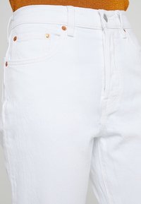 Jeans de mezclilla blanca con corte recto, que cuentan con remaches de cobre, cinco bolsillos y cierre de botón. La tela presenta un acabado texturizado.