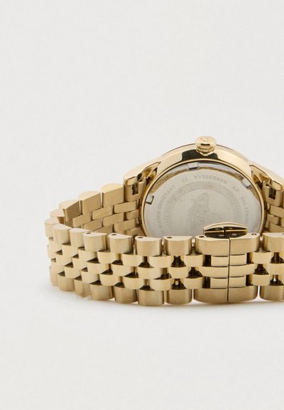 Χρυσός μεταλλικός ιμάντας ρολογιού με διπλωτό κούμπωμα και το πίσω μέρος μιας στρογγυλής χρυσής θήκης ρολογιού ορατό, πάνω σε απλό λευκό φόντο.