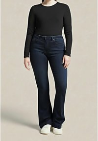 Personne portant un haut noir ajusté à manches longues, un jean évasé taille haute bleu foncé et des chaussures blanches, debout devant un fond uni.