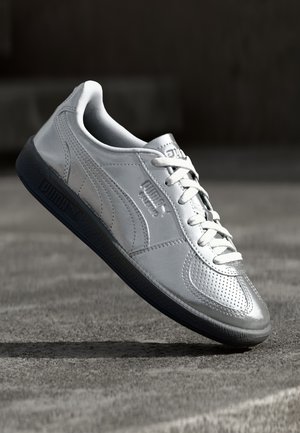 Baskets en cuir gris avec des détails perforés, lacets blancs et semelle texturée bleu marine. Présente le logo Puma sur le côté et sur la languette.