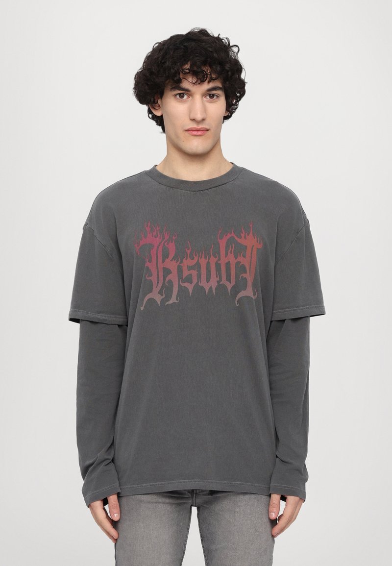 T-shirt gris surdimensionné à manches courtes, avec un graphique au design de flamme en rouge et noir. Le tissu semble doux avec une texture usée.