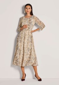 Beige Midikleid mit Schlangenprint, Dreiviertelärmeln, tailliertem Schnitt und fließendem Rock; getragen mit burgunderfarbenen Absätzen.