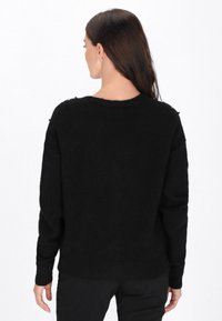 Czarny sweter o luźnym kroju, z okrągłym dekoltem, długimi rękawami i teksturowanymi akcentami na ramionach. Miękki, puszysty materiał.