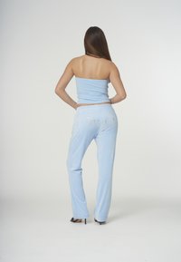 Ljusblå, figurnära axelbandslös topp i kombination med lediga ljusblå byxor. Byxorna har "Juicy" i strass på baksidan. Mjuk textur.