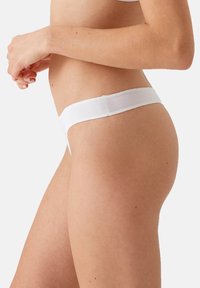 Witte stringonderbroek met een smalle tailleband, gemaakt van een gladde stof. Het ontwerp heeft minimale bedekking met een eenvoudige, naadloze afwerking.