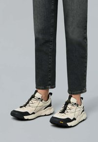Sneakers chunky con una combinazione di colori crema e nero, caratterizzati da una tomaia testurizzata, suola in gomma nera e lacci elastici per una vestibilità sicura.