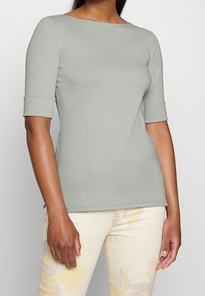 Femme portant un haut cintré à manches courtes gris clair avec des revers pliés et un pantalon clair à motif floral jaune.