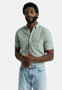 Maglietta a maniche corte a righe verdi e bianche, realizzata in tessuto leggero, con colletto a camicia e taschino sul petto con logo.