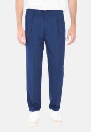 Pantaloni da abito blu navy con una texture liscia, davanti plissettato, passanti per cintura e chiusura a bottone. Indossati con sneakers bianche.