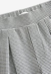Teléfono de tejido de patrón houndstooth en blanco y negro con un ligero brillo; presenta pliegues y una cinturilla plana para un diseño estructurado.