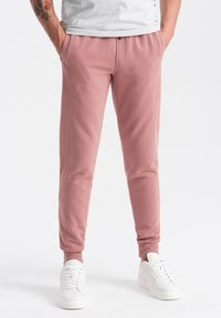 Rosa Jogginghosen aus weichem Material, mit seitlichen Taschen und elastischen Bündchen, kombiniert mit weißen Sneakers für einen sportlichen Look.