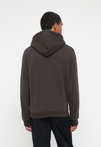 Sweat-shirt capuche marron en tissu doux, offrant une coupe décontractée, des poignets et un ourlet côtelés, avec une couture centrale au dos.