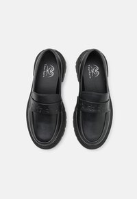 Juodi slip-on batai, pagaminti iš lygaus odos, su žvaigždžių rašto dirželiu, turi storą gumos padą ir apvalią noselę.