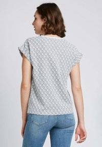 Haut court à manches courtes de couleur blanche avec un motif en losange noir, présentant un col rond et une coupe décontractée. Associé à un jean bleu clair.