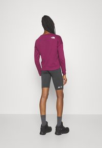Burgunderfärgad sweatshirt med rund hals, grå cykelbyxor, svarta vandringskängor och grå strumpor. Har logodetaljer på sweatshirten och byxorna.