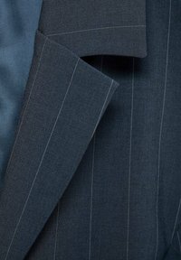 Gros plan sur le col d'une veste de costume bleu foncé à fines rayures blanches verticales et tissu texturé.