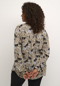 Floral print long-sleeve shirt in khaki, featuring blue and black patterns, a rounded hem, and gathered back detail. Buttons are not visible.