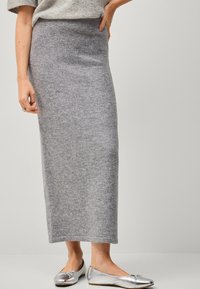 Grijze gebreide maxi rok met een hoge taille en zachte textuur. Gecombineerd met zilveren platte schoenen, tegen een neutrale achtergrond.