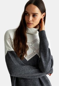Maglione a collo alto lavorato a maglia con un design a blocchi di colore bianco e grigio, motivo decorativo di strass e polsini e collo a coste.