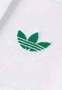 Bijela pamučna ručnik s teksturiranom površinom. Sadrži zeleni logo s izvezenim motivom tri lista i dva horizontalna pruga.