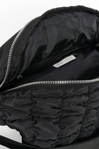 Intérieur d'un sac en nylon noir doté d'une texture matelassée et d'une fermeture éclair argentée. Comprend une poche zippée supplémentaire pour l'organisation.