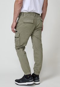 Khaki cargo nohavice s elastickými manžetami, s viacerými vreckami a voľným strihom, skombinované s čiernymi teniskami a vzorovanými ponožkami.