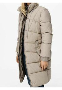 Beige lang polstret pufferjakke med høj krave og klaplommer, båret over en leopardprintet top og blå jeans.