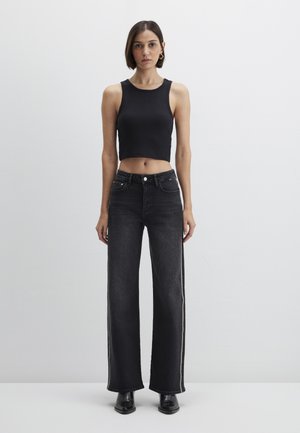 Black ribbed crop top paired with high-waisted, wide-leg black jeans featuring white side stripes. Black ankle boots complete the outfit.