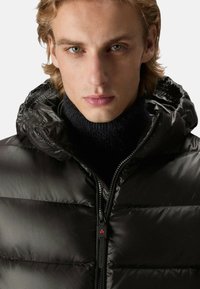 Zwarte pufferjas met een glanzende afwerking, ritssluiting en capuchon. Met een getextureerde gebreide coltrui eronder voor extra warmte.