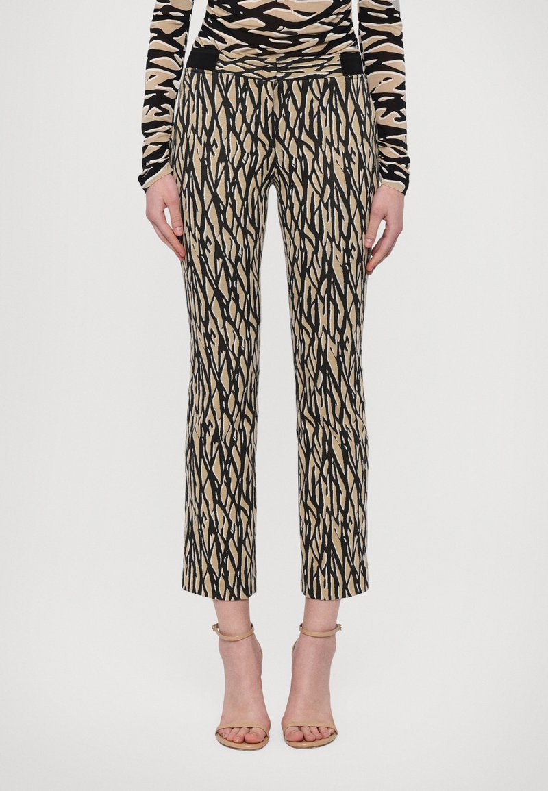 Trousers featuring a bold black and beige zigzag pattern, made from a smooth fabric, with a fitted waist and cropped hem.