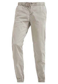 Ljust beige, bomullsblandade byxor med elastisk midja, dragskoöppning och smalnande bendesign. Slät textur, inga framträdande mönster.