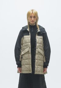 Επενδυμένο μπουφάν με αντίθετες μαύρες και μπεζ πάνελ, διαθέτοντας κουκούλα, πολλές τσέπες και φερμουάρ για ζεστασιά και λειτουργικότητα.