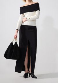 Black off-the-shoulder sweater paired with a high-slit black skirt. Model holds a black suede bag, wearing black heeled mules with pointed toes.