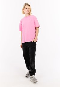 Roze katoenen oversized t-shirt met korte mouwen en een ronde halslijn, gecombineerd met een zwarte corduroy broek en grijze sportschoenen.