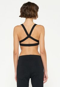 Sujeción deportiva negra con tirantes anchos en cruz en la parte posterior. Textura suave y diseño ajustado, combinado con pantalones negros de tiro alto.