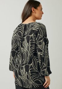 Blusa nera con maniche lunghe, caratterizzata da un motivo astratto a foglia color crema. Tessuto testurizzato con un dettaglio arricciato sul retro per un design aggiuntivo.