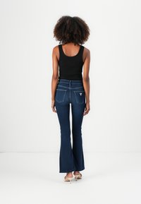 Jean évasé bleu foncé à taille haute, avec deux poches arrière et un détail logo en triangle. Assorti avec un top noir ajusté.