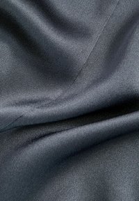 Tessuto di satin grigio scuro con una texture liscia, caratterizzato da un leggero luccichio e da pieghe drappeggiate che mettono in evidenza la fluidità del materiale.