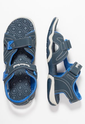 Kindersandalen in Marineblau und Weiß mit verstellbaren Riemen und strukturierten Innensohlen mit sechseckigem Muster, gezeigt aus der Vogelperspektive und von der Seite.