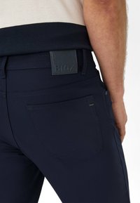 Pantalon bleu marine au toucher lisse, arborant une étiquette en cuir à la taille arrière et une poche sur le côté droit.