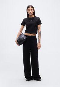 Μαύρο cropped t-shirt με το λογότυπο CK, σε συνδυασμό με μαύρο παντελόνι ψηλόμεσο και με φαρδιά μπατζάκια. Υφή τσαντάκι clutch σε μαύρο και κομψά μαύρα παπούτσια.