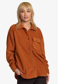 Orange fleece shirt with a button front, pointed collar, and a single pocket. Soft texture and relaxed fit with rounded hem.