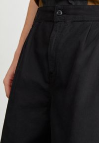 Czarne spodnie wykonane z lekkiego materiału, z zapięciem na guzik, gładką fakturą i subtelnymi detalami przeszyć.