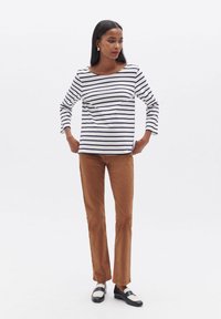 Gestreiftes Langarmoberteil in Weiß und Marineblau, kombiniert mit braunen Slim-Fit-Hosen. Die Schuhe sind schwarz mit weißen Akzenten. Einfaches, tailliertes Design.