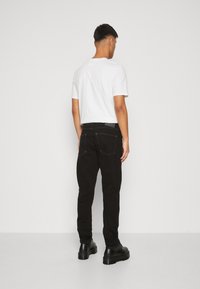 Vaqueros de mezclilla negra con corte recto, detalles de costura sutil y un diseño de bolsillo trasero. Complementados con una camiseta de algodón blanca lisa.