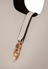 Gros plan d’un sac en cuir texturé beige avec intérieur noir et détail de fermoir en métal doré sur la bandoulière près de la découpe de la poignée.