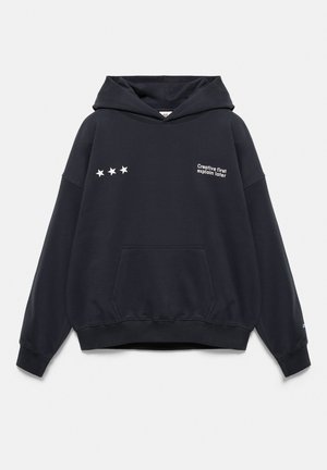 Sweat à capuche noir avec poche avant, trois étoiles blanches sur la poitrine gauche et la phrase "Creative first explain later" sur la poitrine droite.